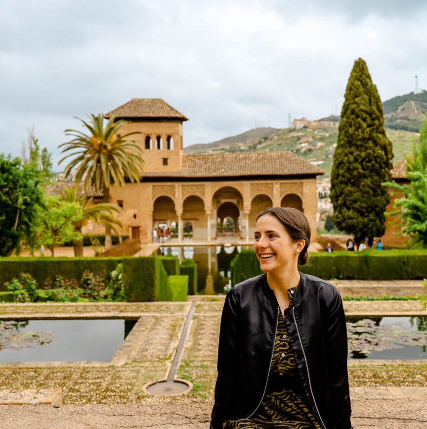 frau sitzt vor gebaeude in der alhambra in andalusien