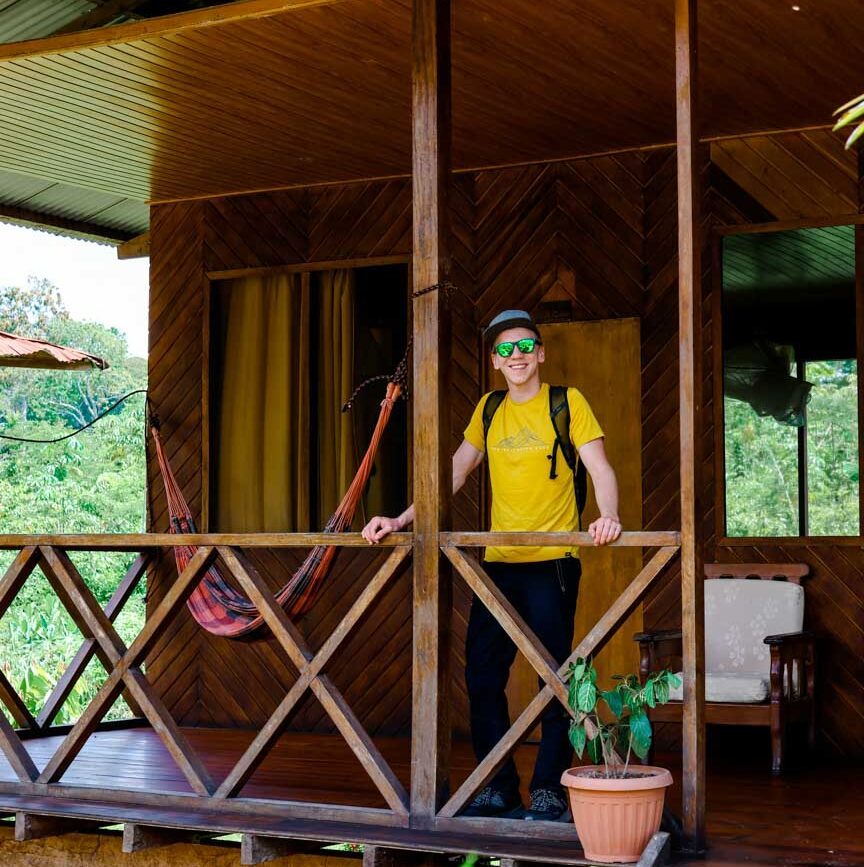 mann auf der veranda eines hoelzernen amazonas hauses