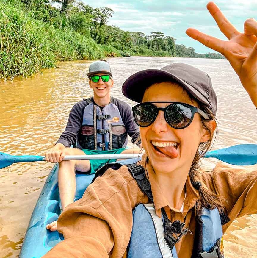 zwei menschen im kanu durch amazonas und machen ein friedenszeichen