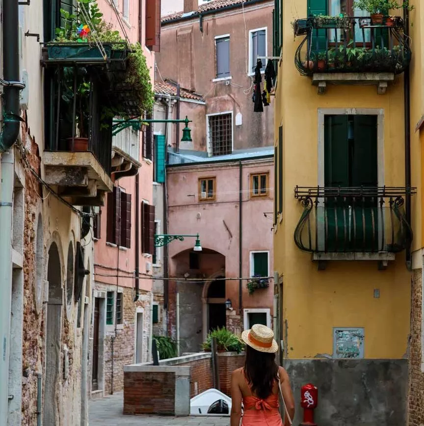 Frau in Hut läuft durch enge Gasse in Venedig