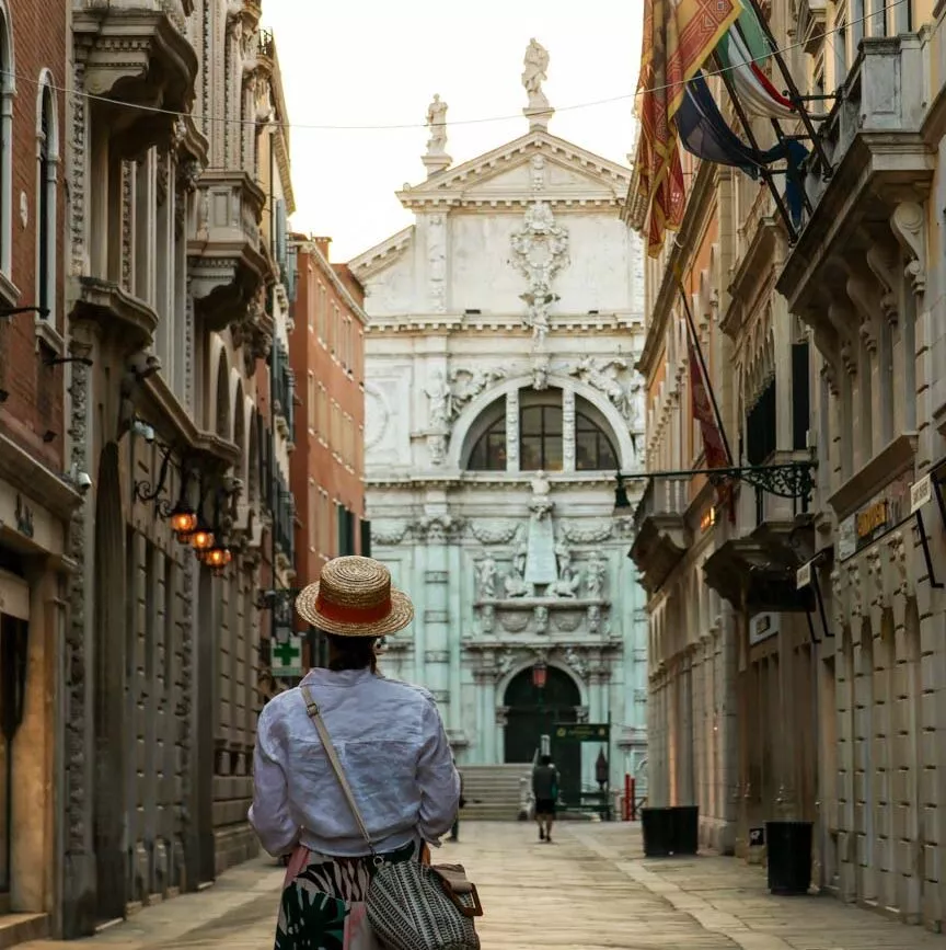 Person im Strohhut sieht weißes Gebäude in Venedig