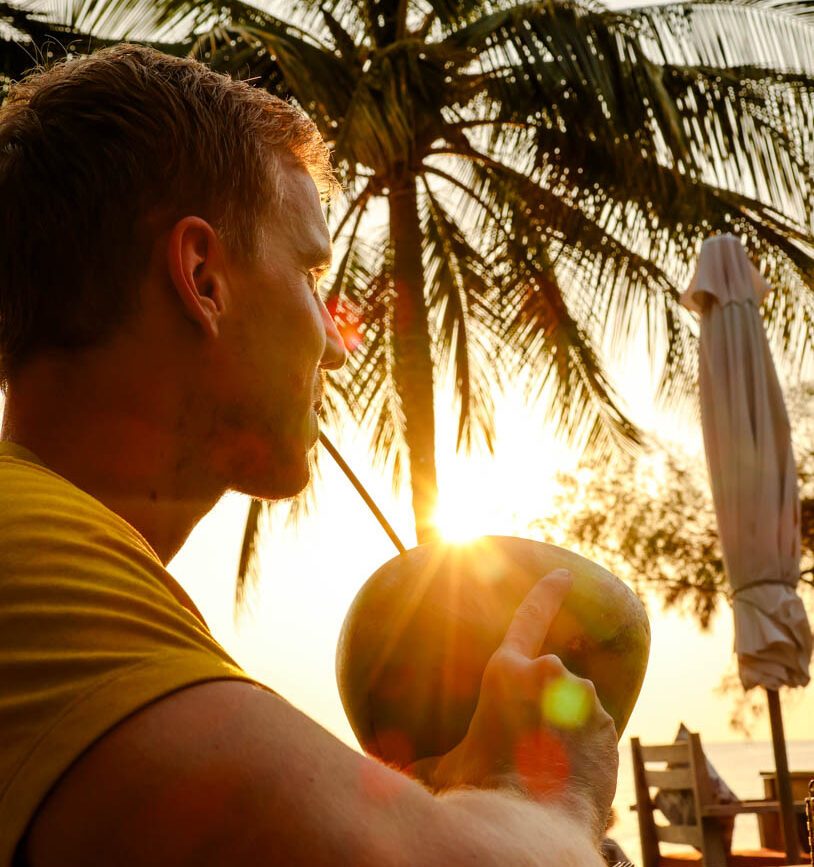 tom schluerft kokosnuss bei sonnenuntergang