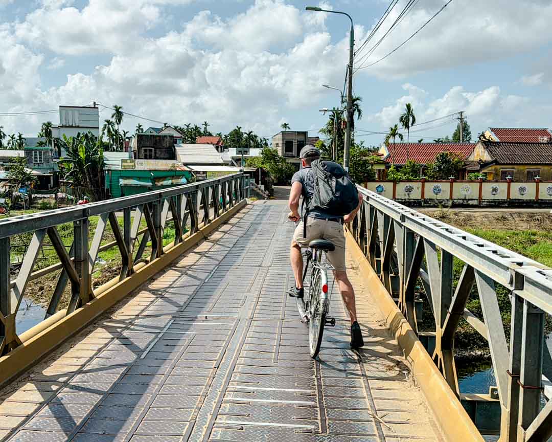 tom faehrt mit fahrrad ueber bruecke in hoi an vietnam