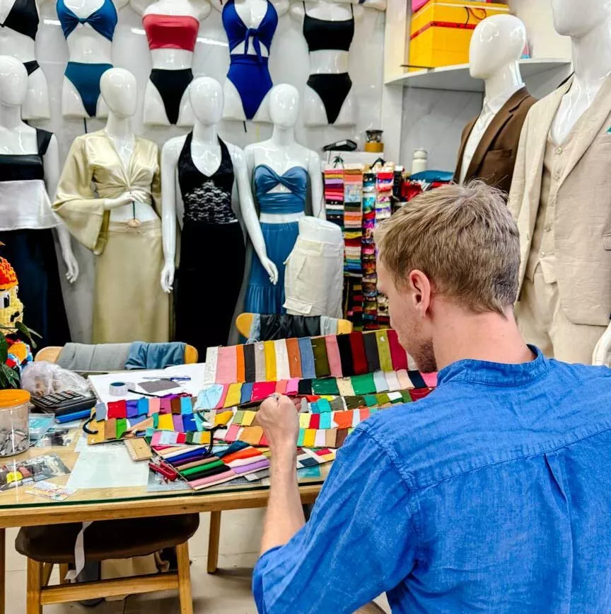 tom schaut stoffmuster an im tailor shop in hoi an