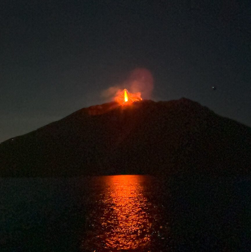 Der Vulkan Stromboli bricht nachts aus und die Lava spiegelt sich im Wasser