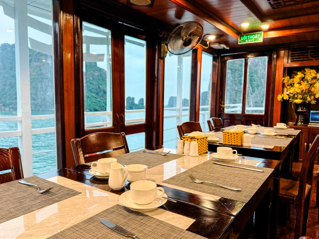 Essbereich auf dem Boot mit gedeckten Tischen und Blick auf die Halong-Bucht