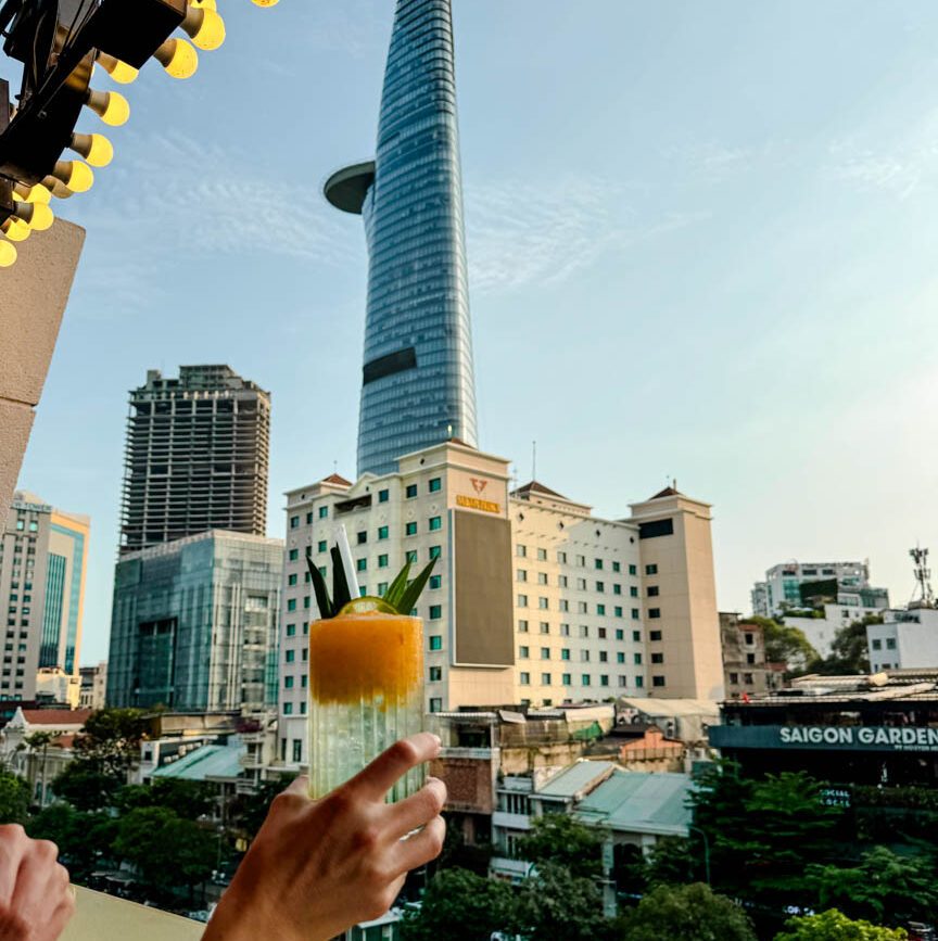 hand haelt cocktail vor der skyline von ho chi minh stadt