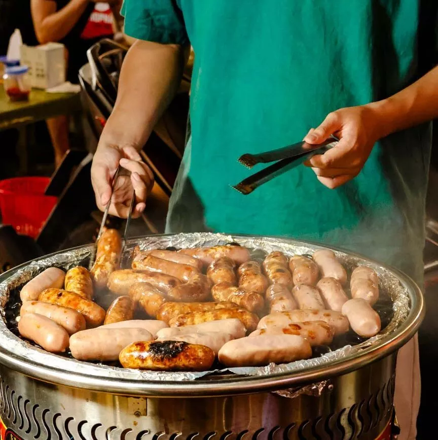person grillt wuerstchen auf rundem grill Person grillt Würstchen auf rundem Grill