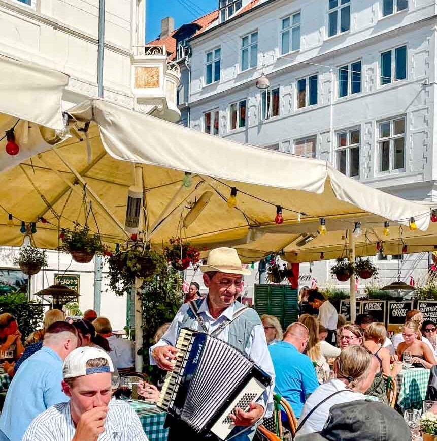 Akkordeonspieler zwischen den Restauranttischen am Neuen Hafen in Kopenhagen, Dänemark